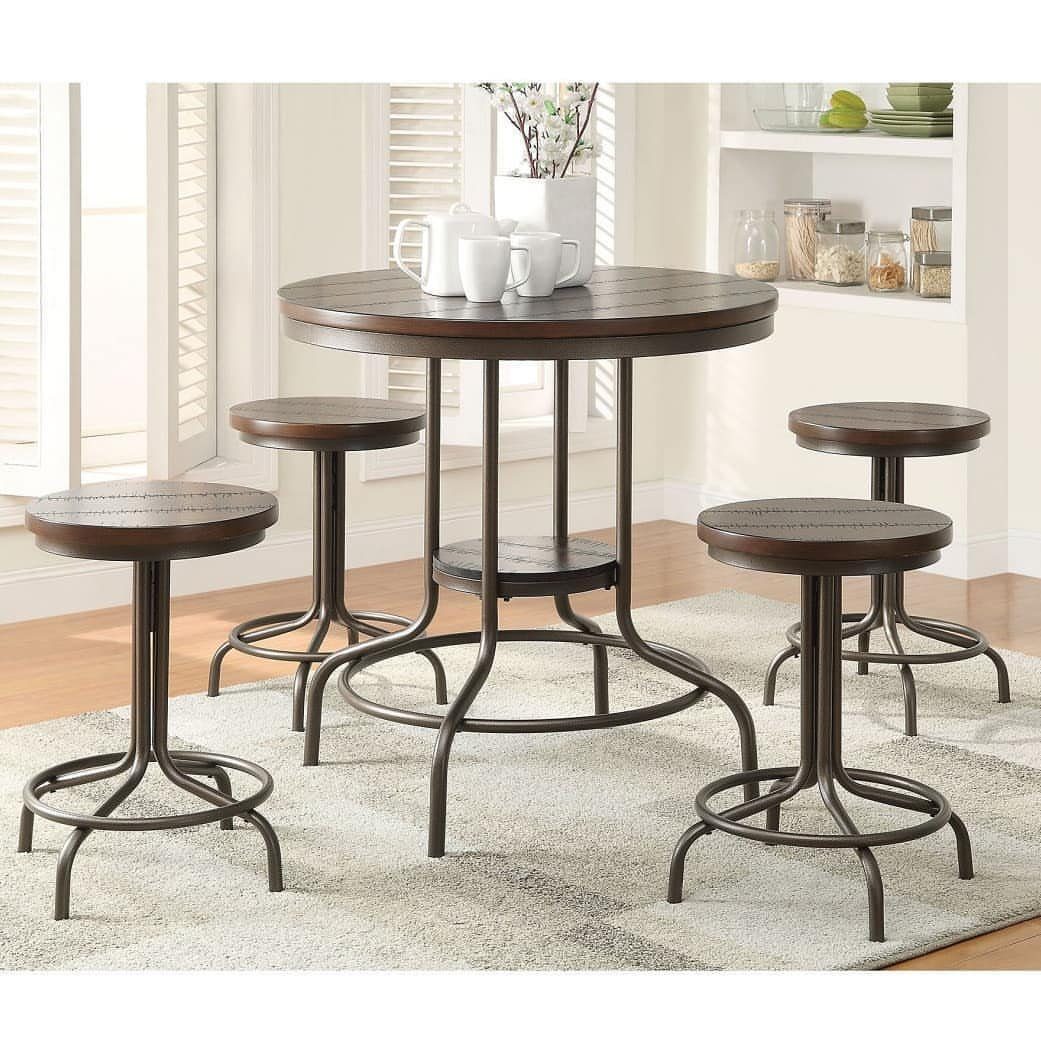 Round dark wood counter-height dining table with four matching backless stools on a rug.
