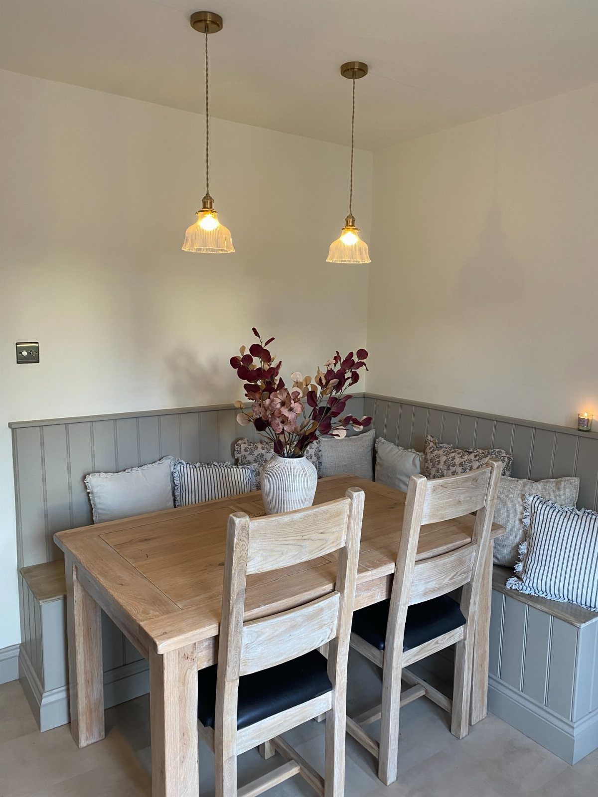 L-shaped grey corner dining bench with a light wood table and chairs.