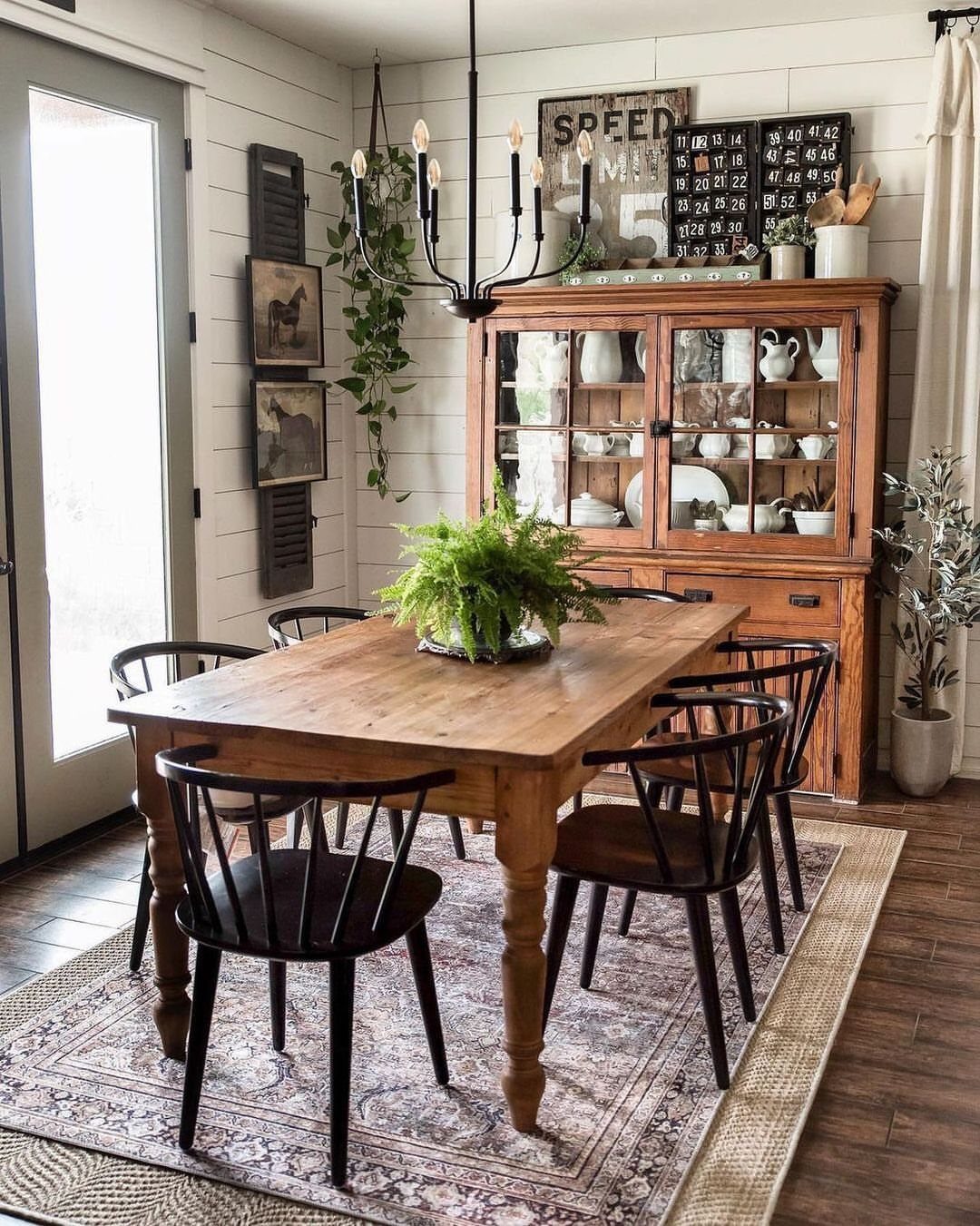 Black spindle-back dining chairs surrounding a light wood farmhouse table in a rustic room.