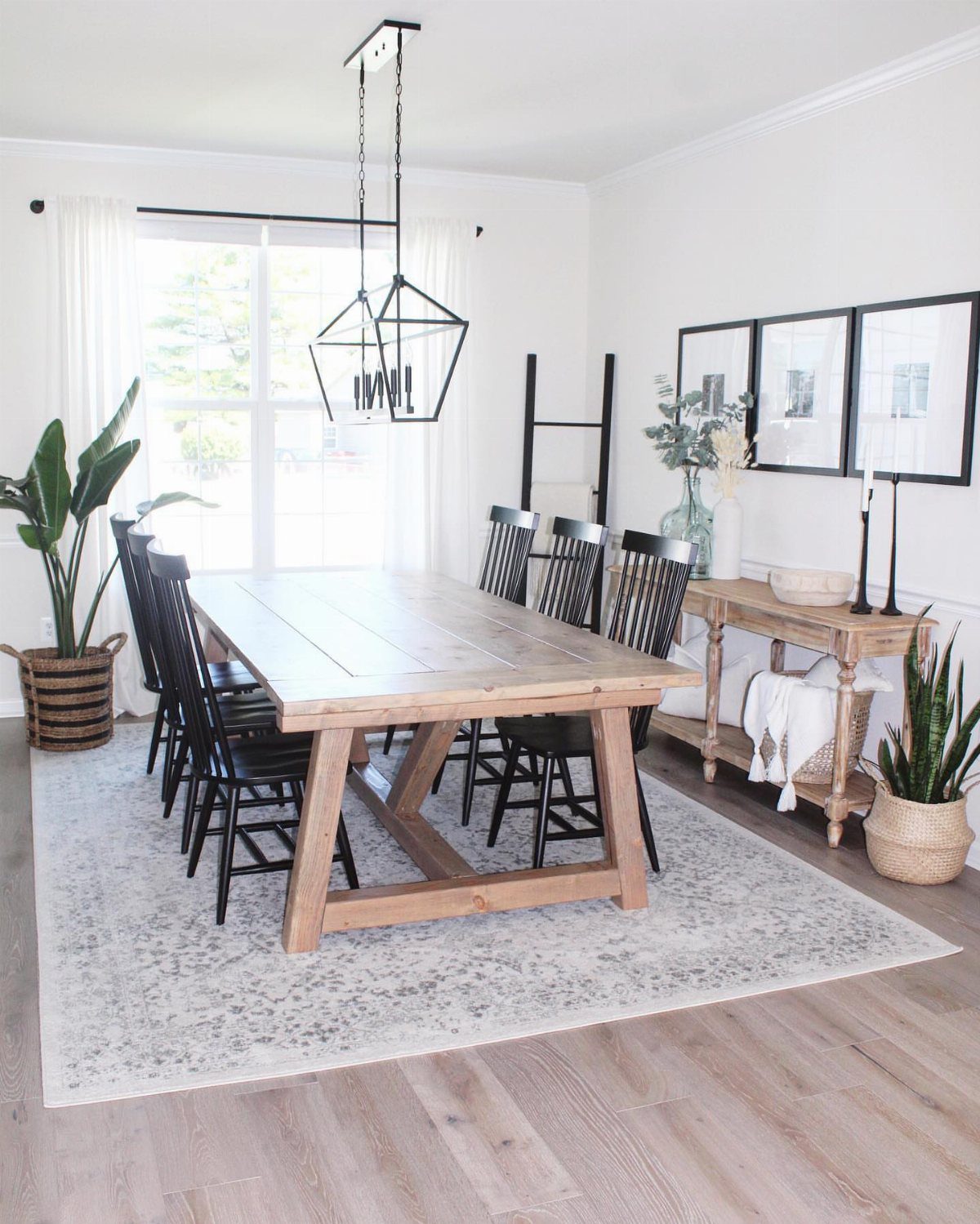 Light wood farmhouse dining table with black chairs in a bright, modern room.