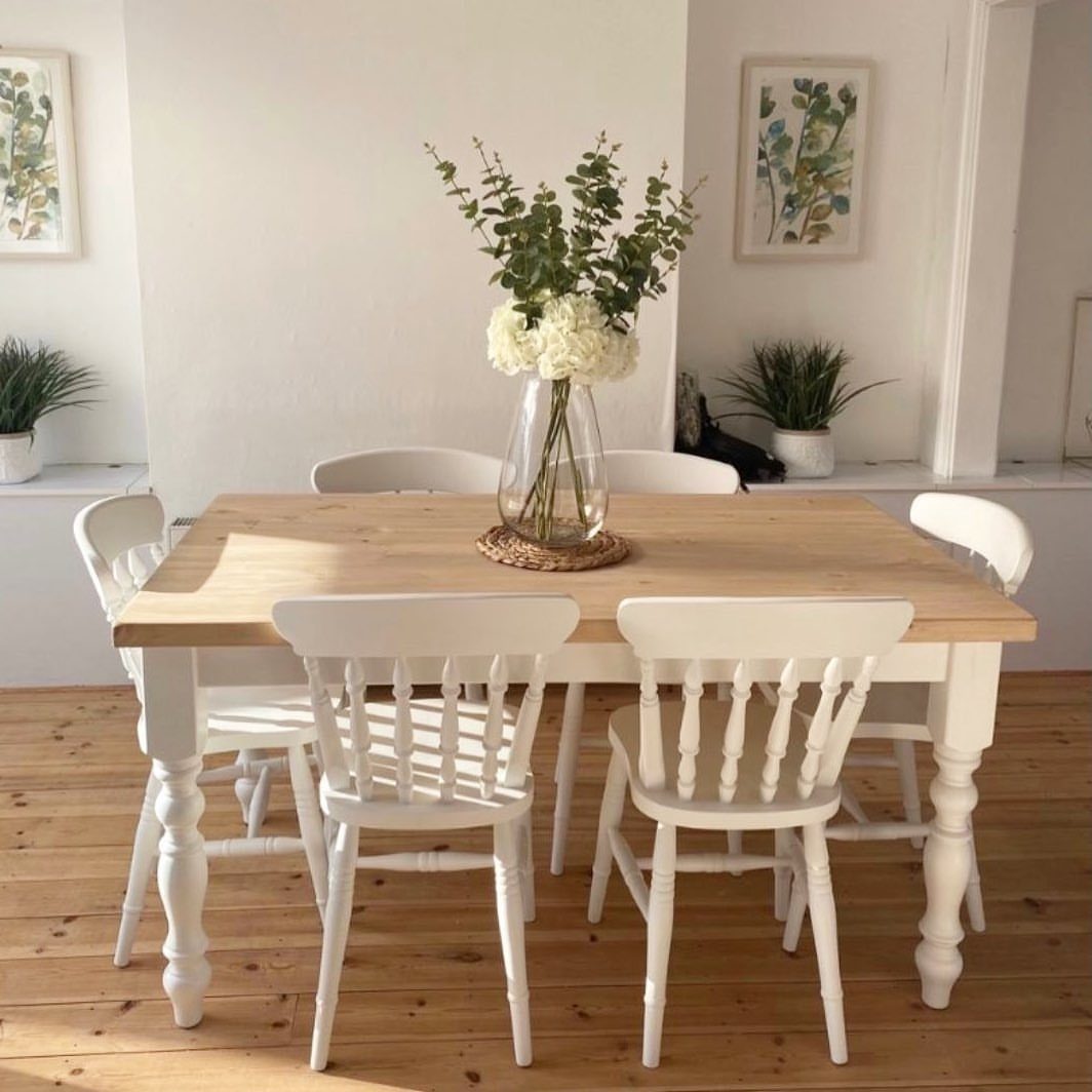 Wooden dining table with white legs and matching white spindle-back chairs in bright room.
