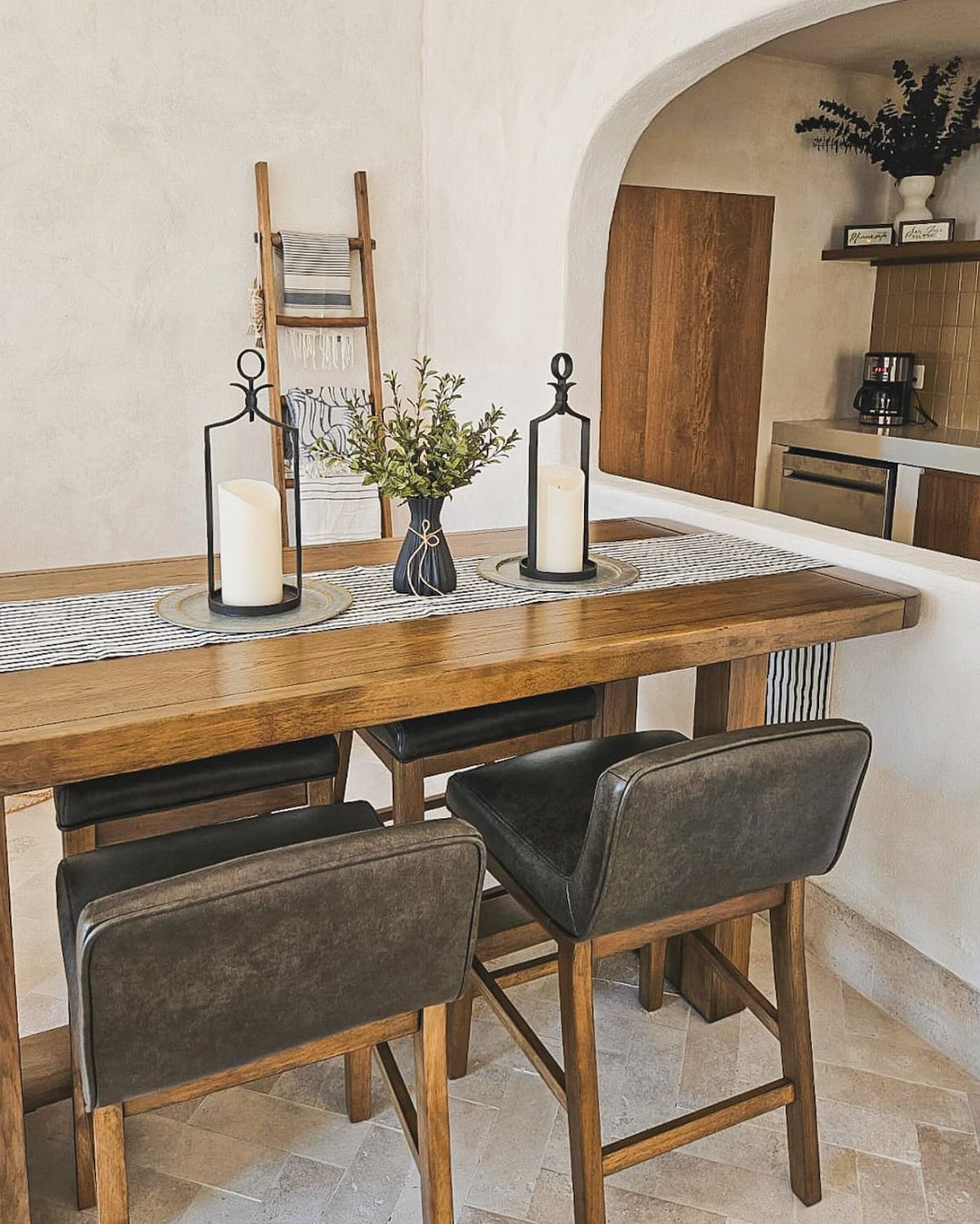 Rustic wooden dining table with dark leather chairs and candle lanterns in a room.
