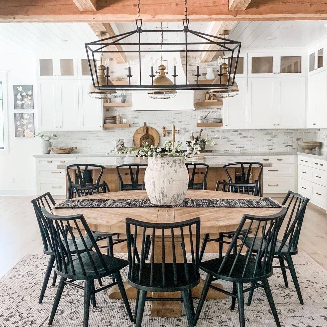 Round wooden dining table with black spindle chairs in a bright farmhouse kitchen
