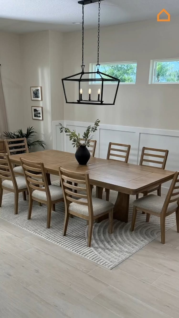 Rectangular light wood dining table with matching chairs under a black lantern chandelier.