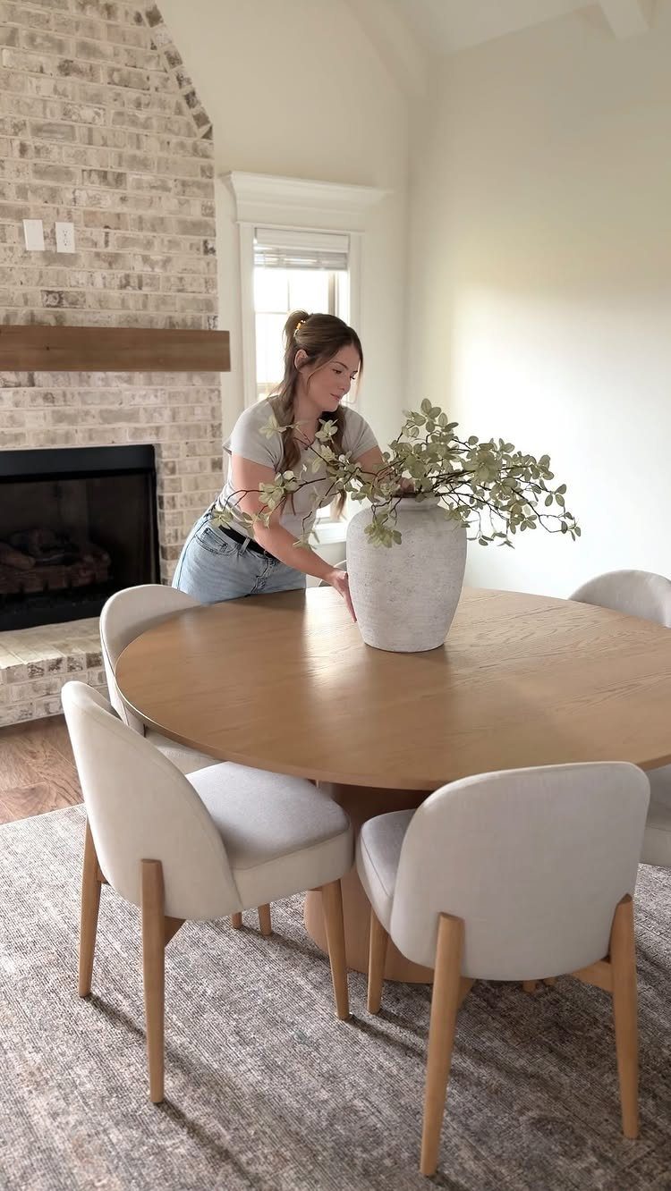 Round light-wood pedestal dining table with white upholstered chairs in a bright room.