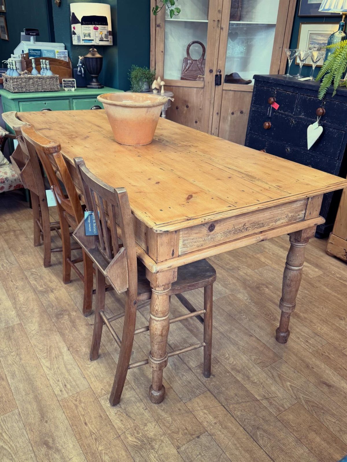Rectangular wooden farmhouse dining table with matching chairs and a terracotta bowl.