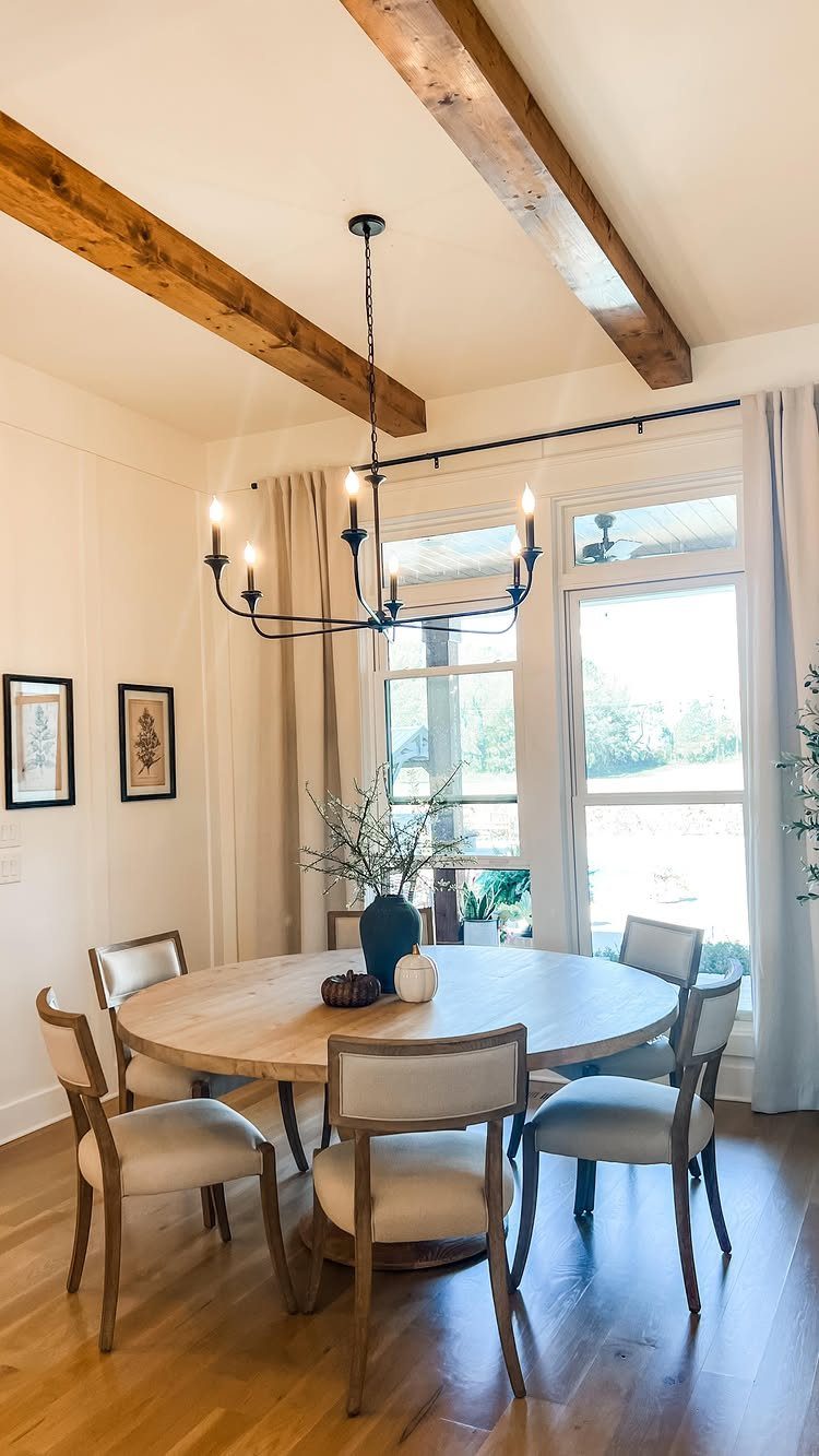 Round light-wood dining table with four cream upholstered chairs under a black chandelier.