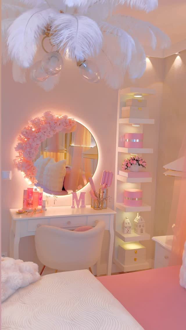 White vanity desk with round mirror and feather chandelier in pink bedroom.
