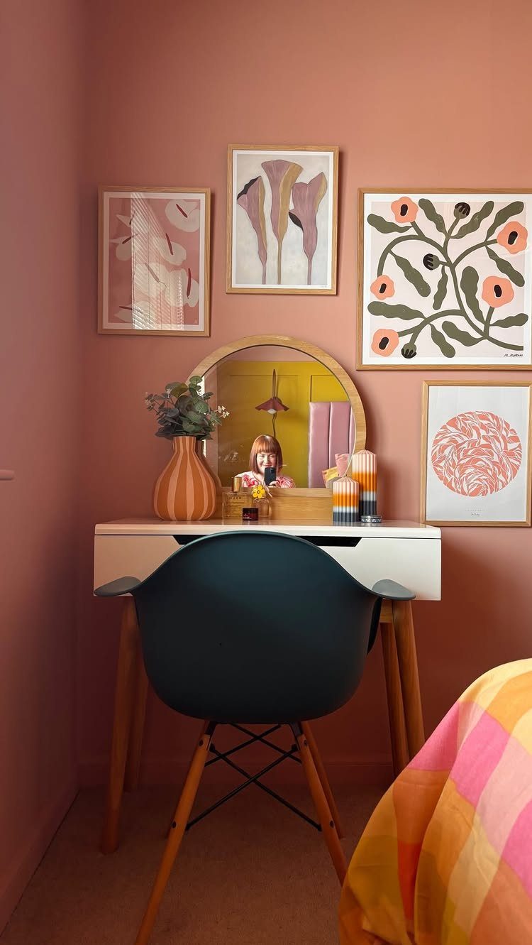 Four framed art prints arranged on a terracotta wall above a white desk.