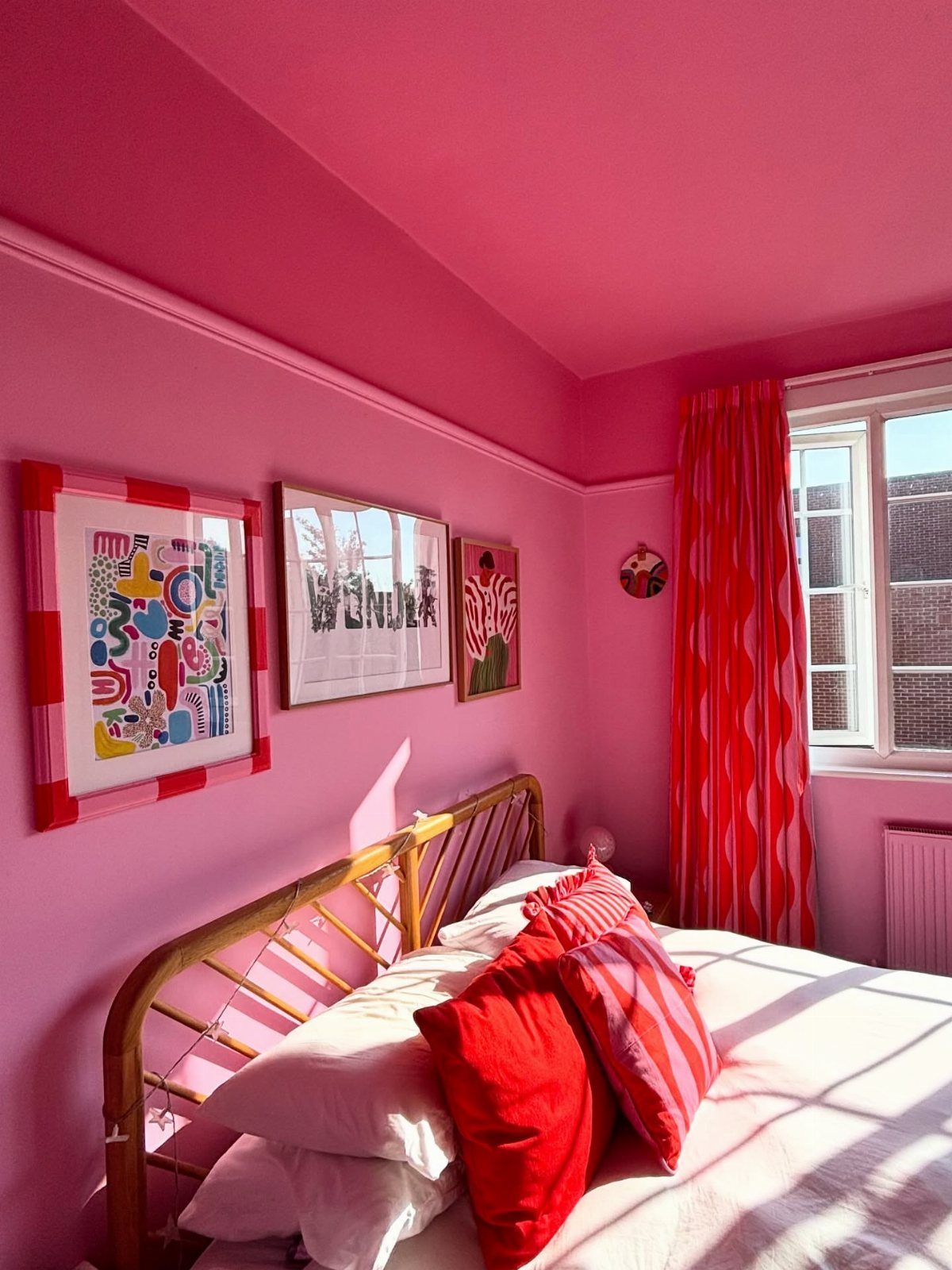 Bright pink bedroom with a matching pink painted ceiling and red accent pillows.