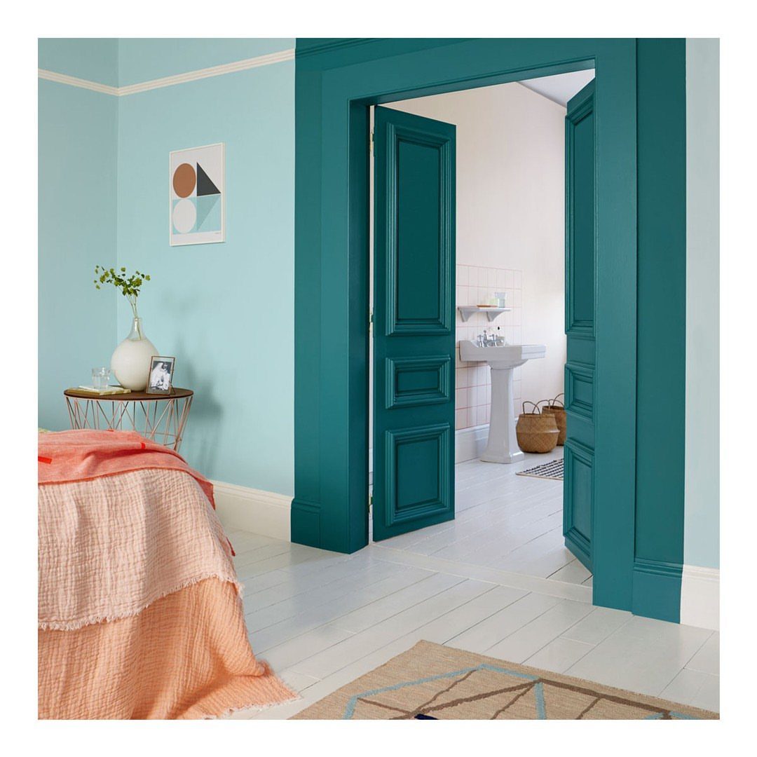 Pale blue bedroom walls with a turquoise door frame and orange bedding.