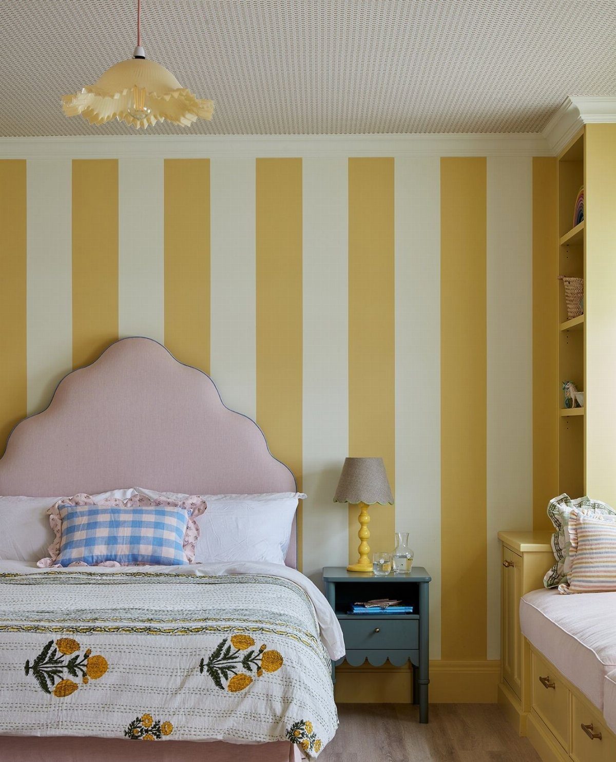 Bedroom with pink scalloped headboard and yellow and white striped wallpaper.