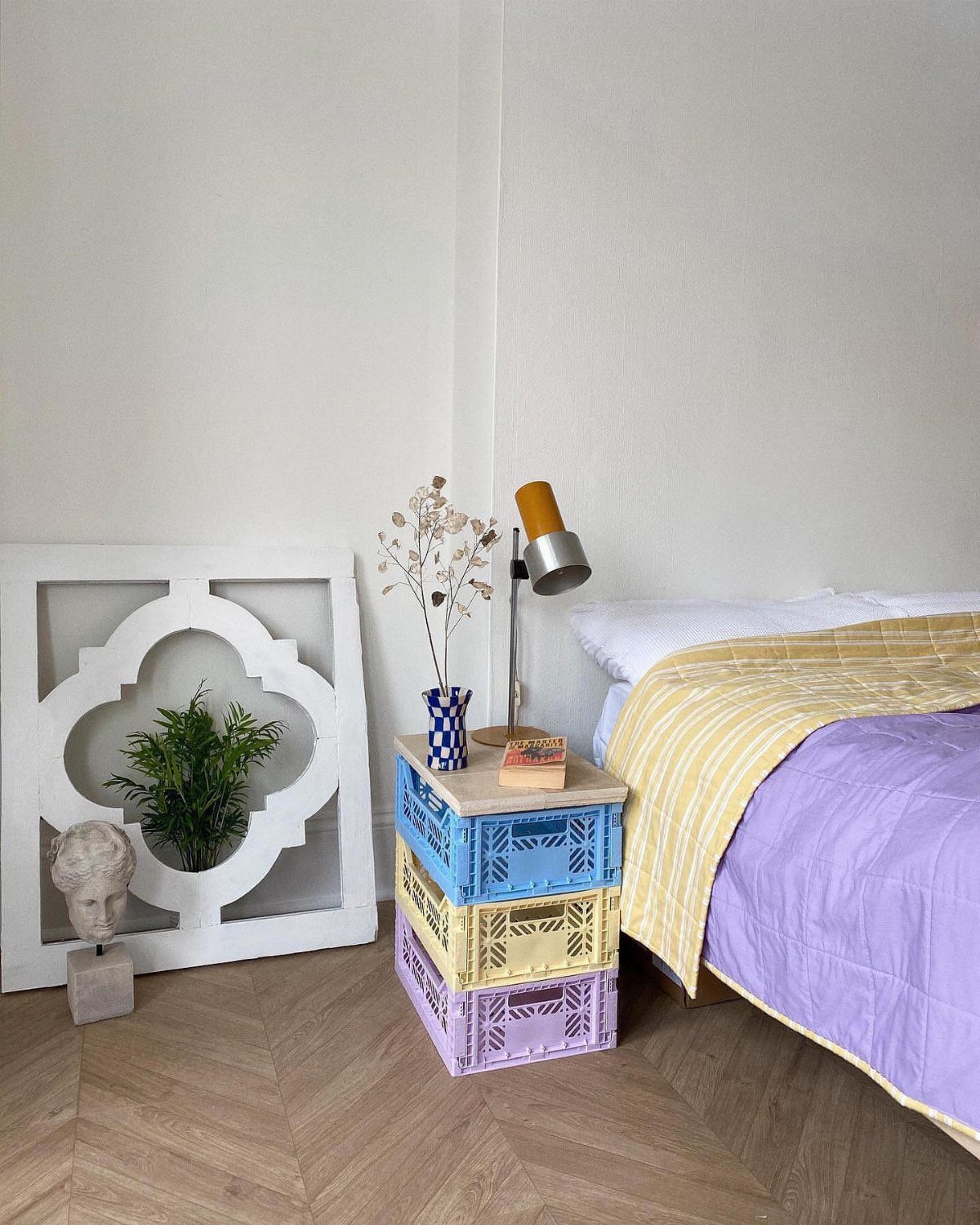 Bed with purple and yellow linens next to a colorful stacked crate nightstand.