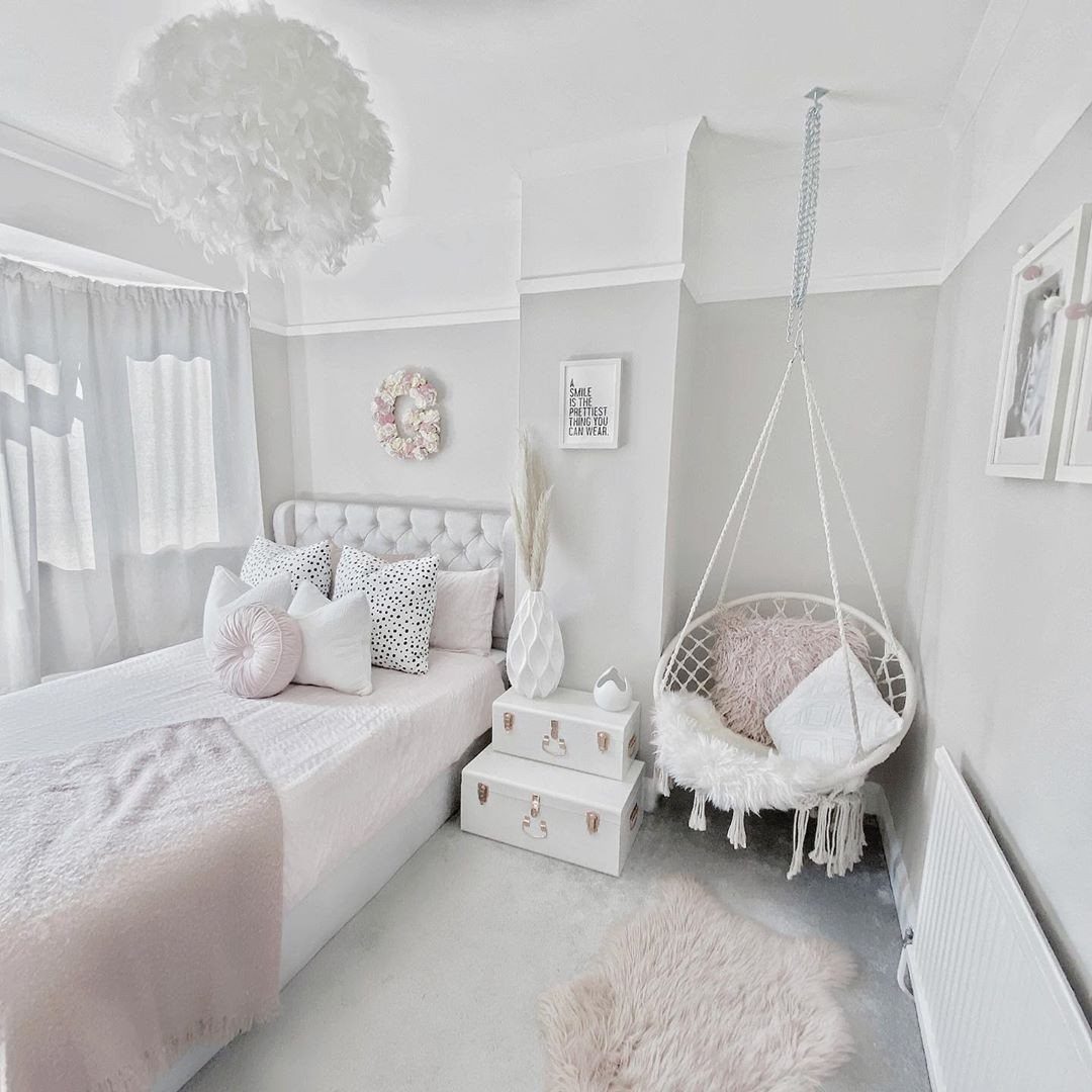 White hanging egg swing chair with pillows in a light gray girl's bedroom.