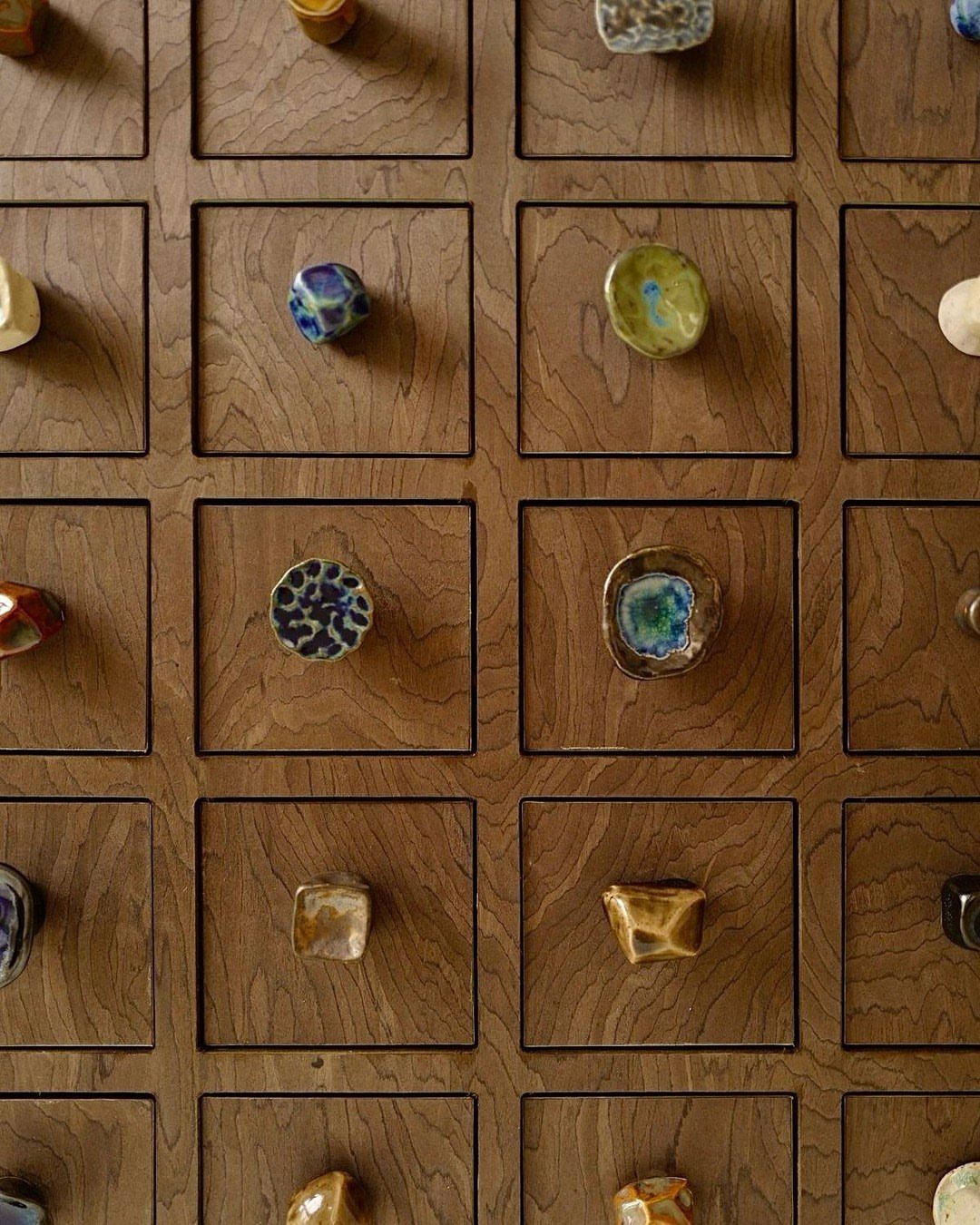 Colorful ceramic cabinet knobs on a grid of small wooden drawers.