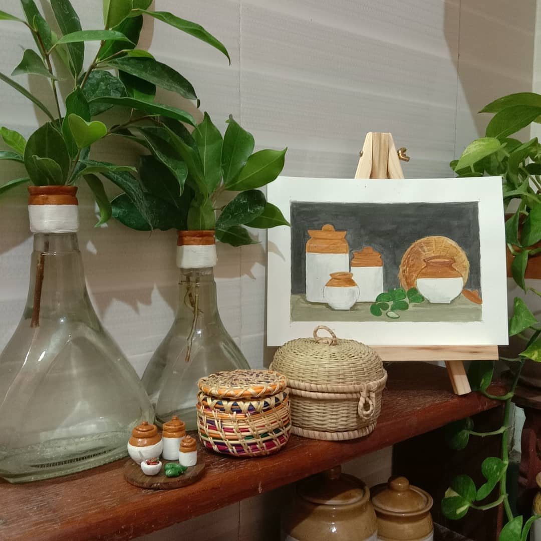 Wooden shelf with plants, woven baskets, and a painting of traditional Indian pots.