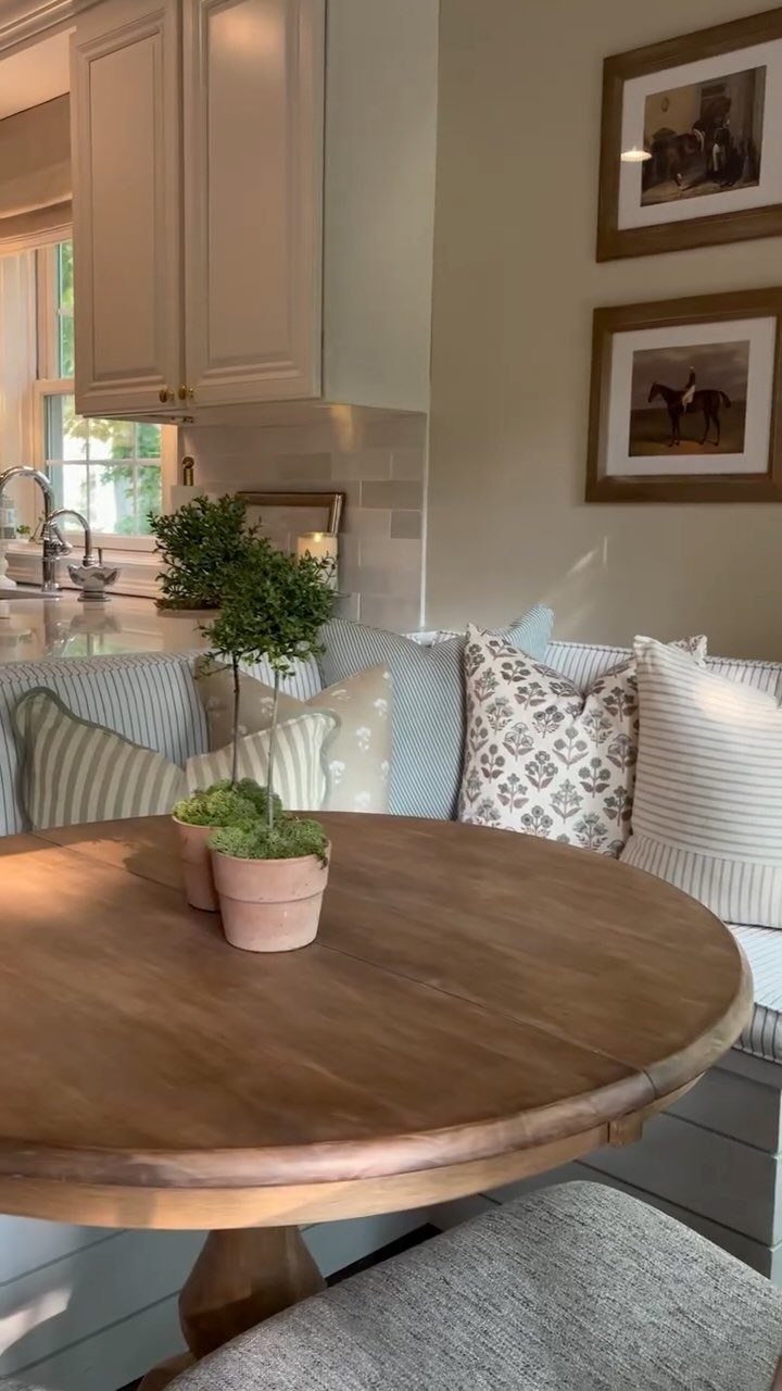 Round wooden dining table with a built-in banquette seat and decorative pillows.