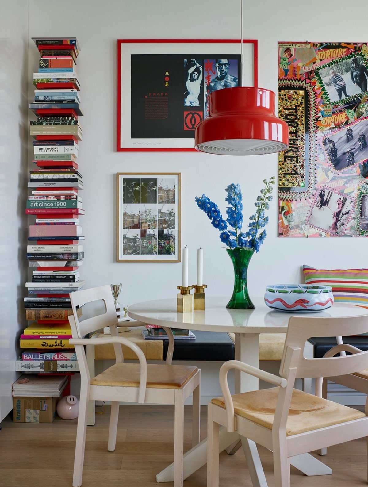 Eclectic dining room with a round white table, red lamp, and colorful wall art.