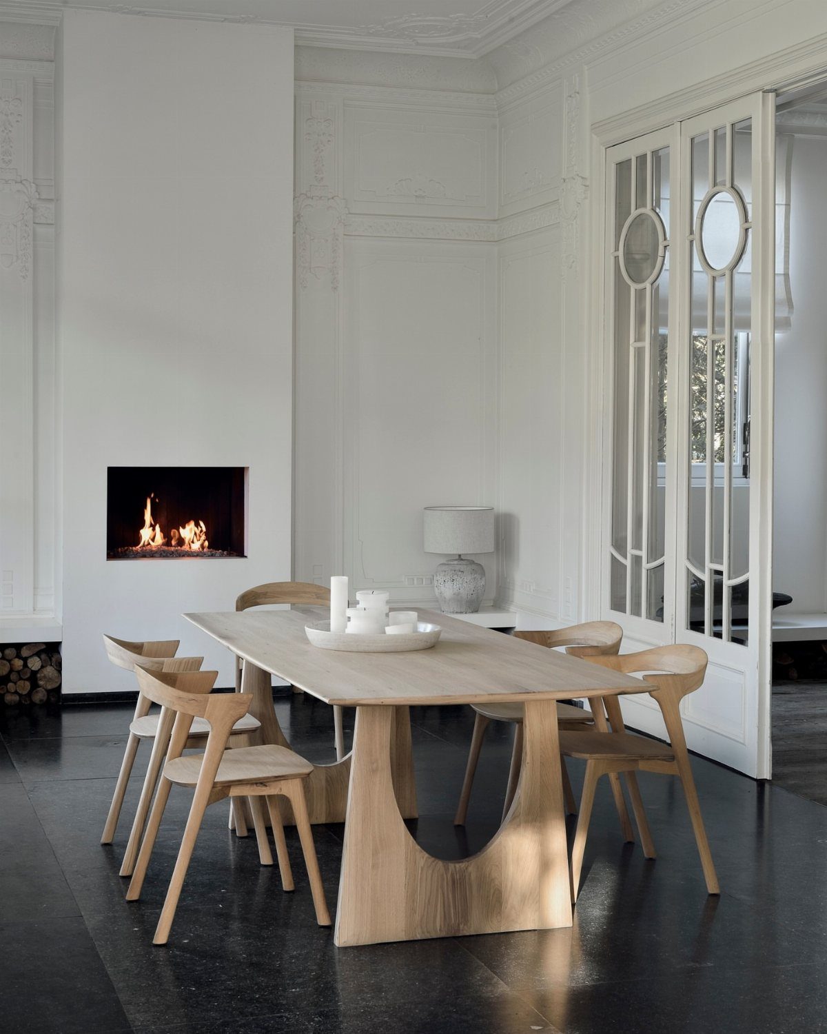 Wooden dining table with a geometric pedestal base and matching chairs in white room.