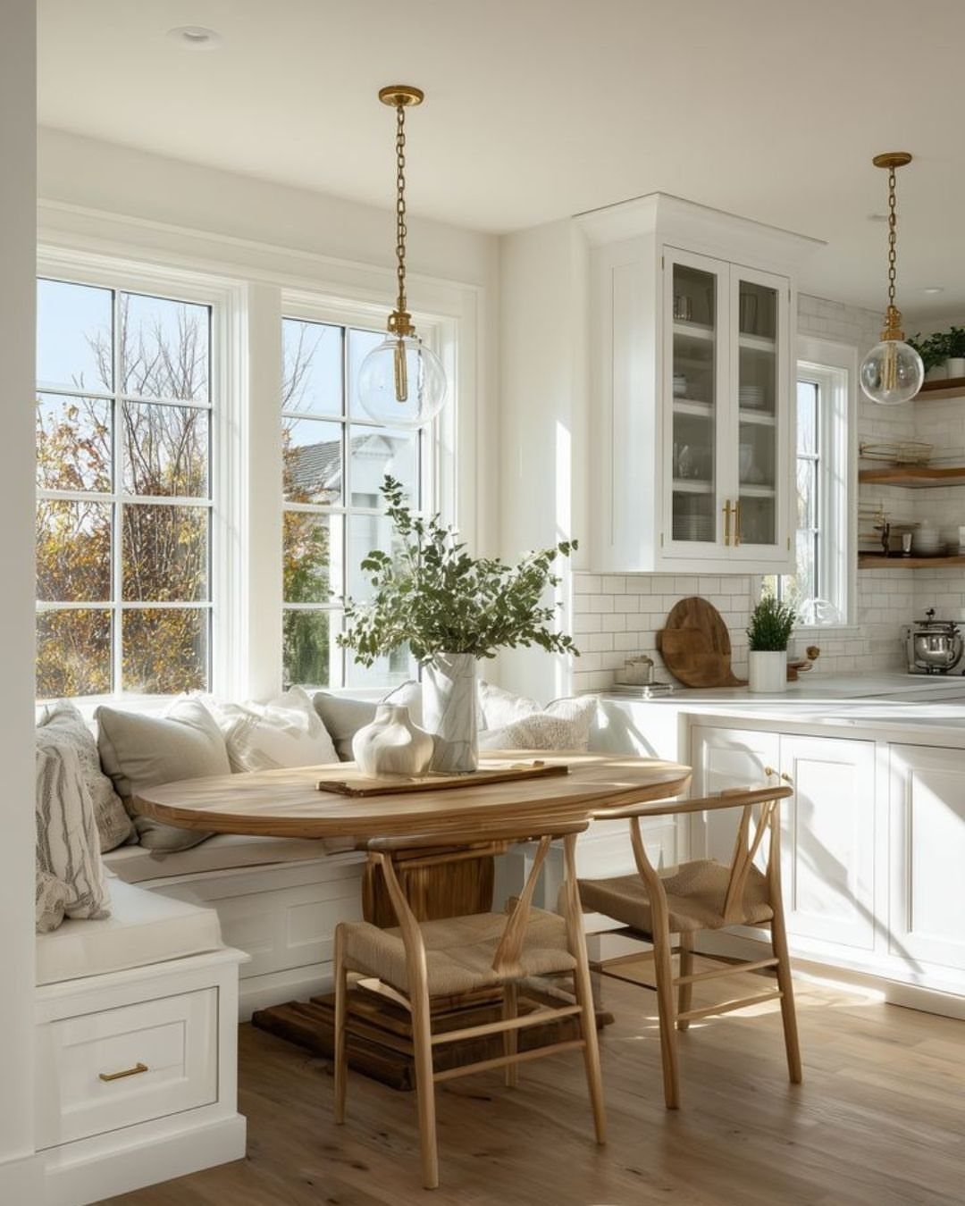Round wooden table and built-in banquette seating in a bright white kitchen nook.