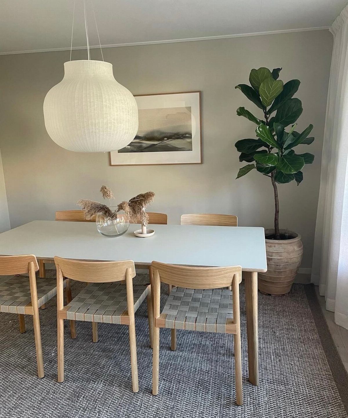 White rectangular dining table with woven chairs and a large white pendant light.