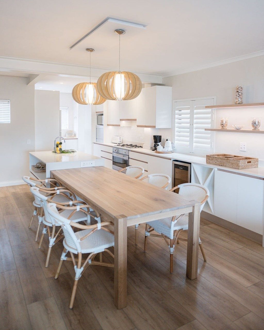 Wooden dining table with white woven chairs in a bright open-plan kitchen area