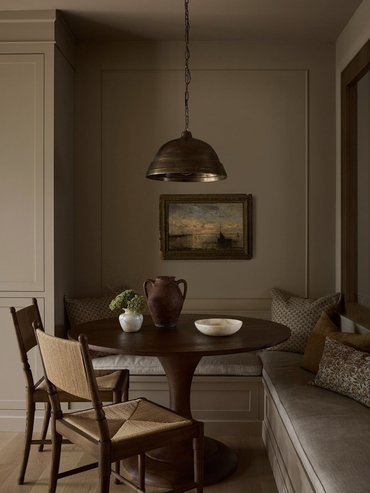 Round dark wood dining table with pedestal base and built-in banquette seating.
