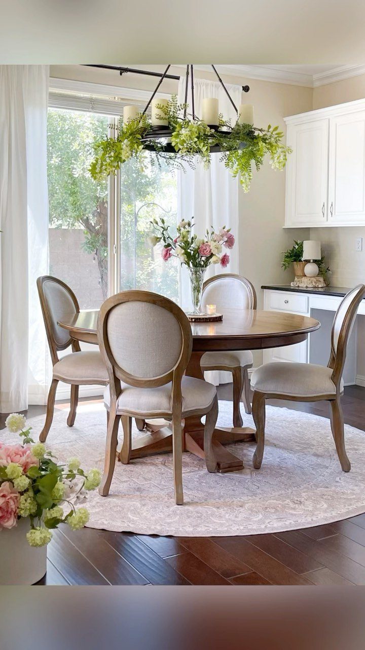 Round wooden dining table with oval-backed chairs on a circular rug in bright room