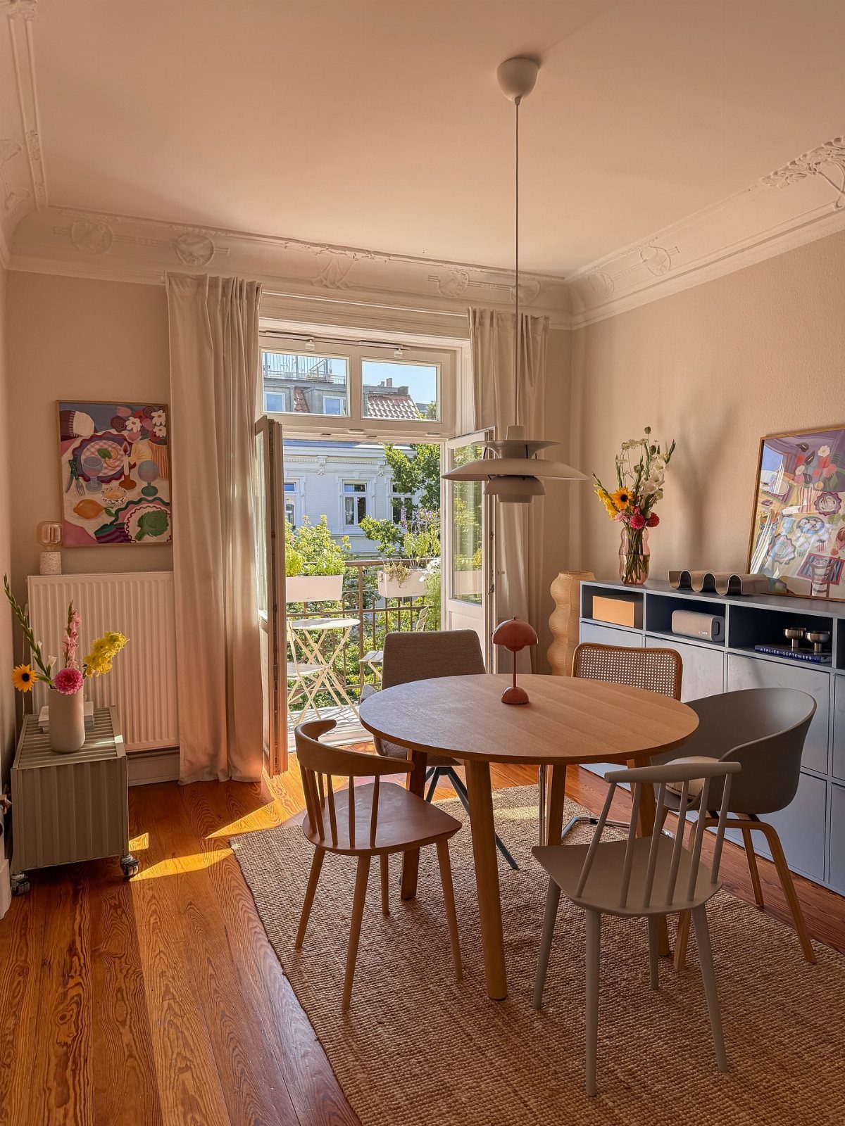 Round wooden dining table with mismatched chairs on a jute rug in a bright room.