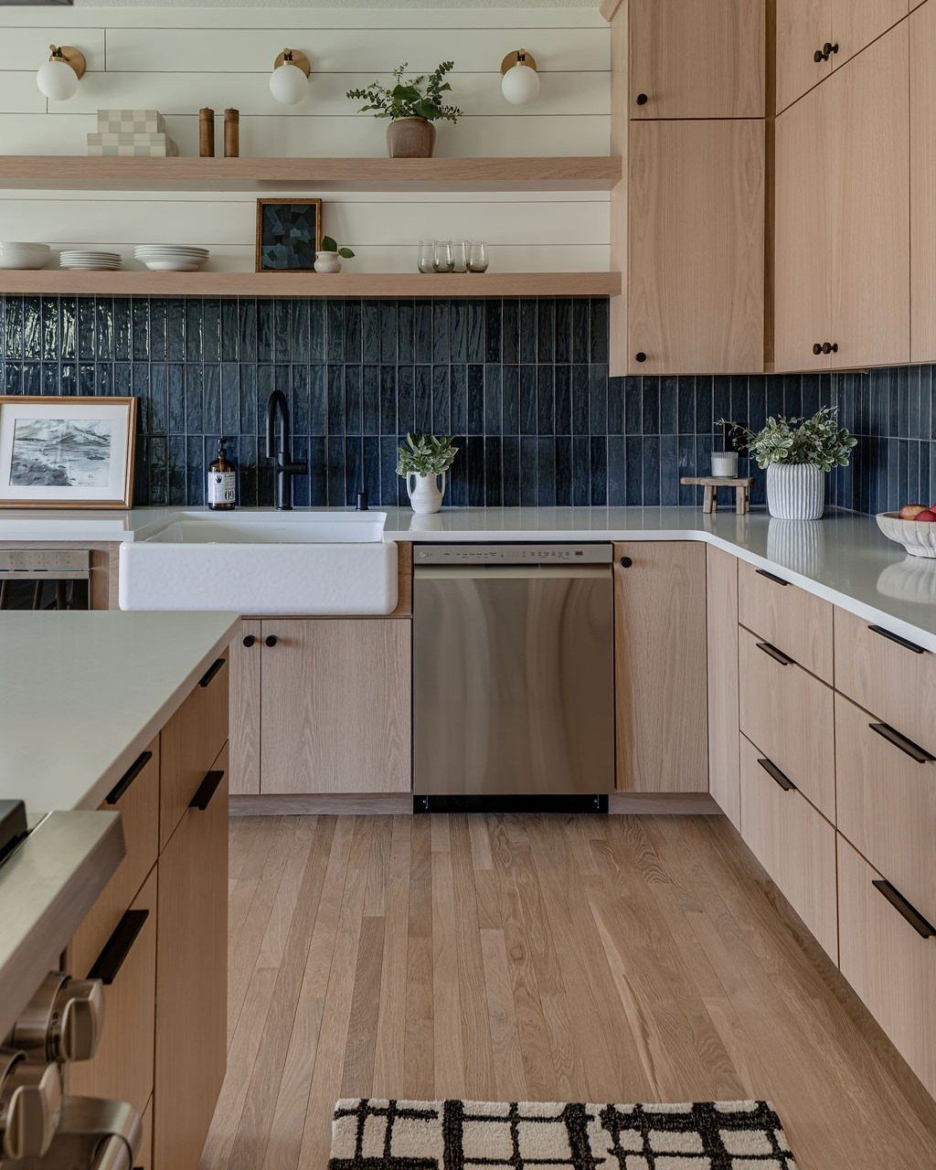 Modern kitchen with light wood cabinets, white farmhouse sink, and dark blue tile backsplash.