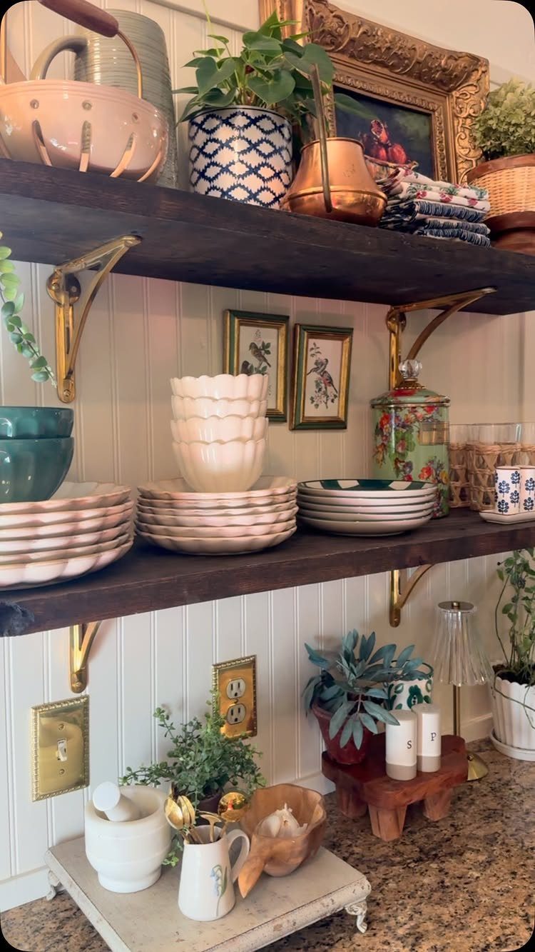 Dark wood open shelves with gold brackets holding ceramic dishes and potted plants.