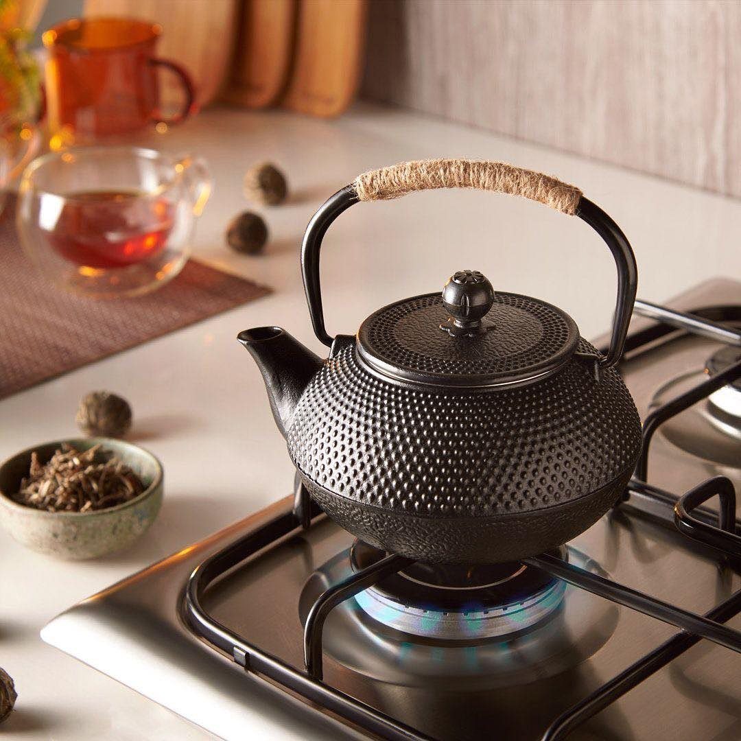 Black cast iron Japanese teapot heating on a gas stove burner in a kitchen.