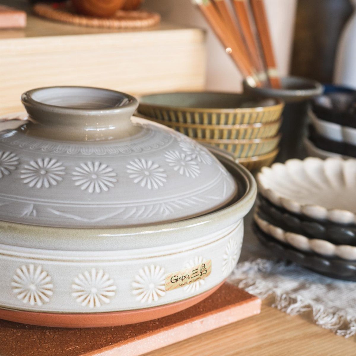 Light grey ceramic donabe clay pot with floral patterns on a terracotta trivet.