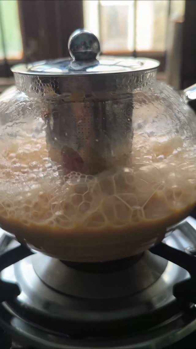 Glass teapot with metal strainer and bubbling tea on a gas stove.