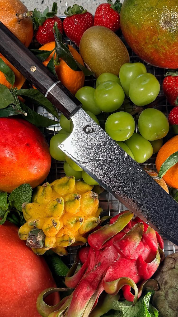 Japanese chef's knife resting on a colorful assortment of fresh tropical fruits.