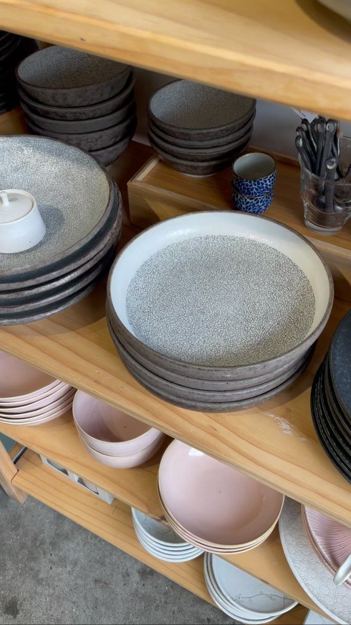 Stacks of ceramic plates and bowls in neutral tones on wooden shelves.