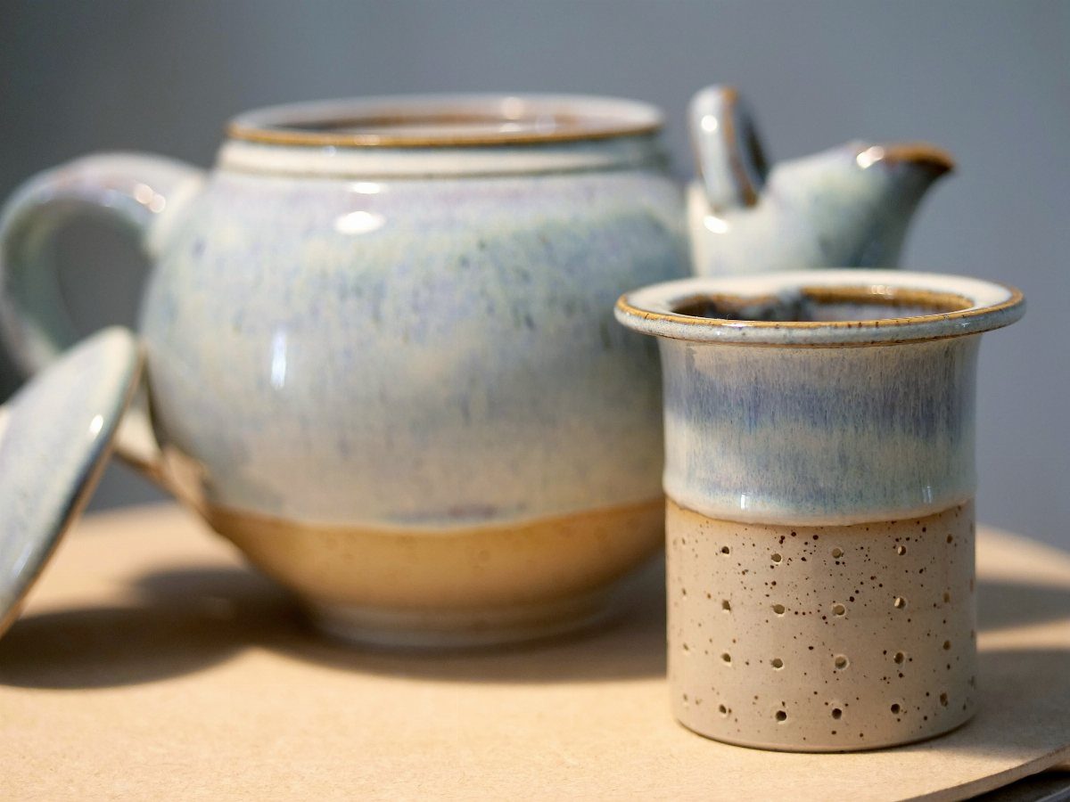 Ceramic teapot and matching tea strainer with light blue and tan glazes.