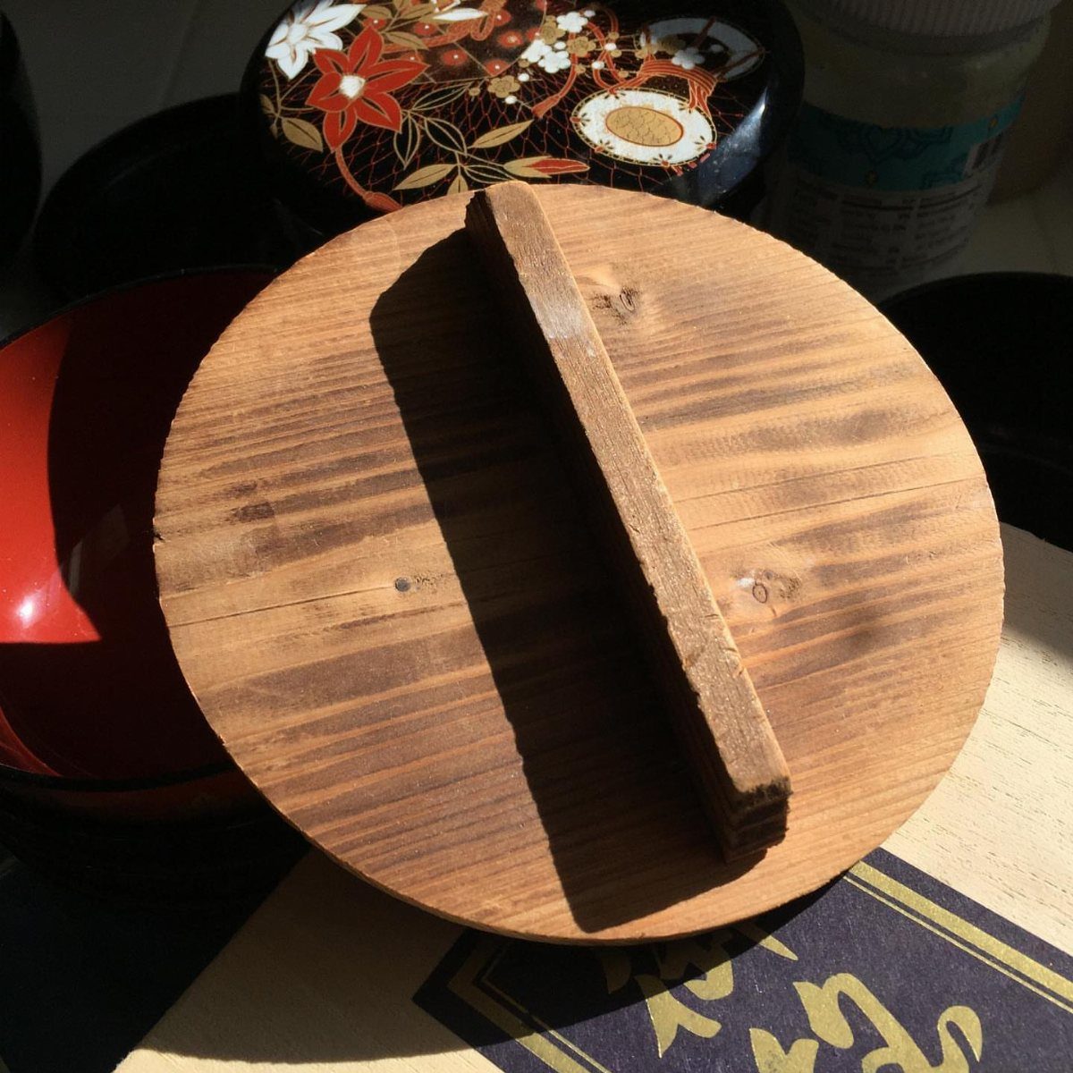 Wooden otoshibuta drop lid with a central handle resting on a kitchen surface