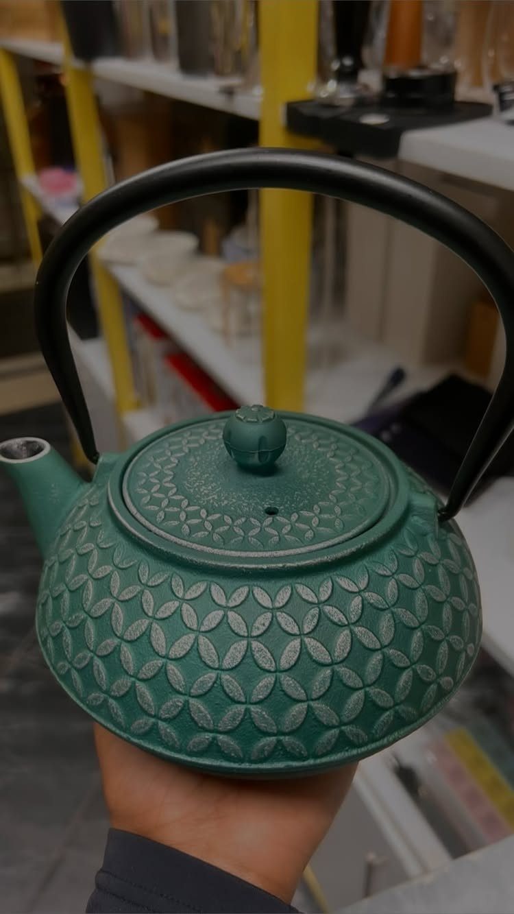 Green cast iron Japanese teapot with textured pattern and black handle held by hand.