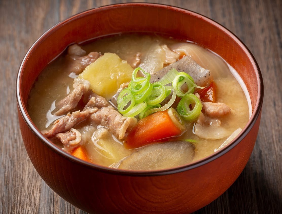 Wooden miso soup bowl filled with meat, vegetables, and sliced green onions.