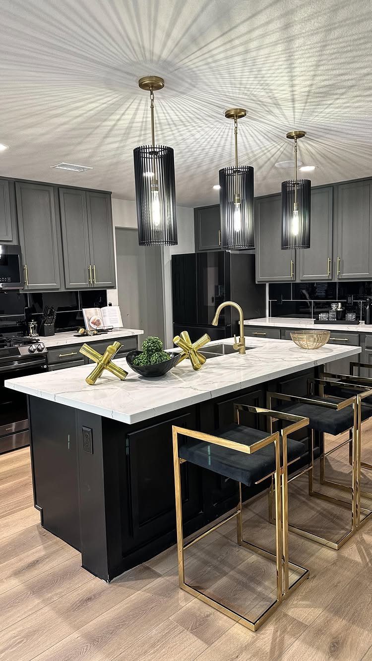 Dark gray kitchen cabinets and island with white marble countertops and gold bar stools.