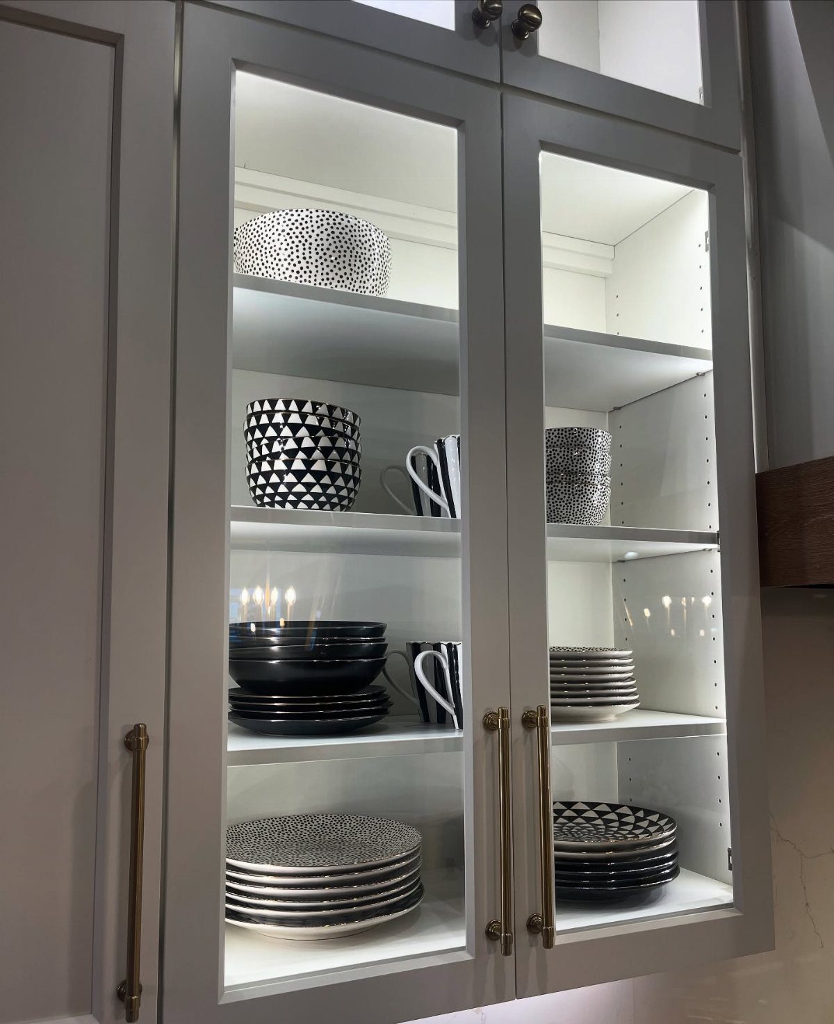 White kitchen cabinets with glass doors displaying black and white dinnerware and interior lighting.