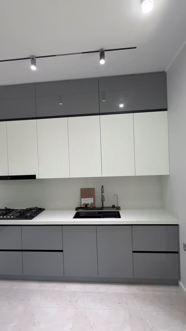 Modern kitchen with gray and white cabinets, white countertop and black appliances.