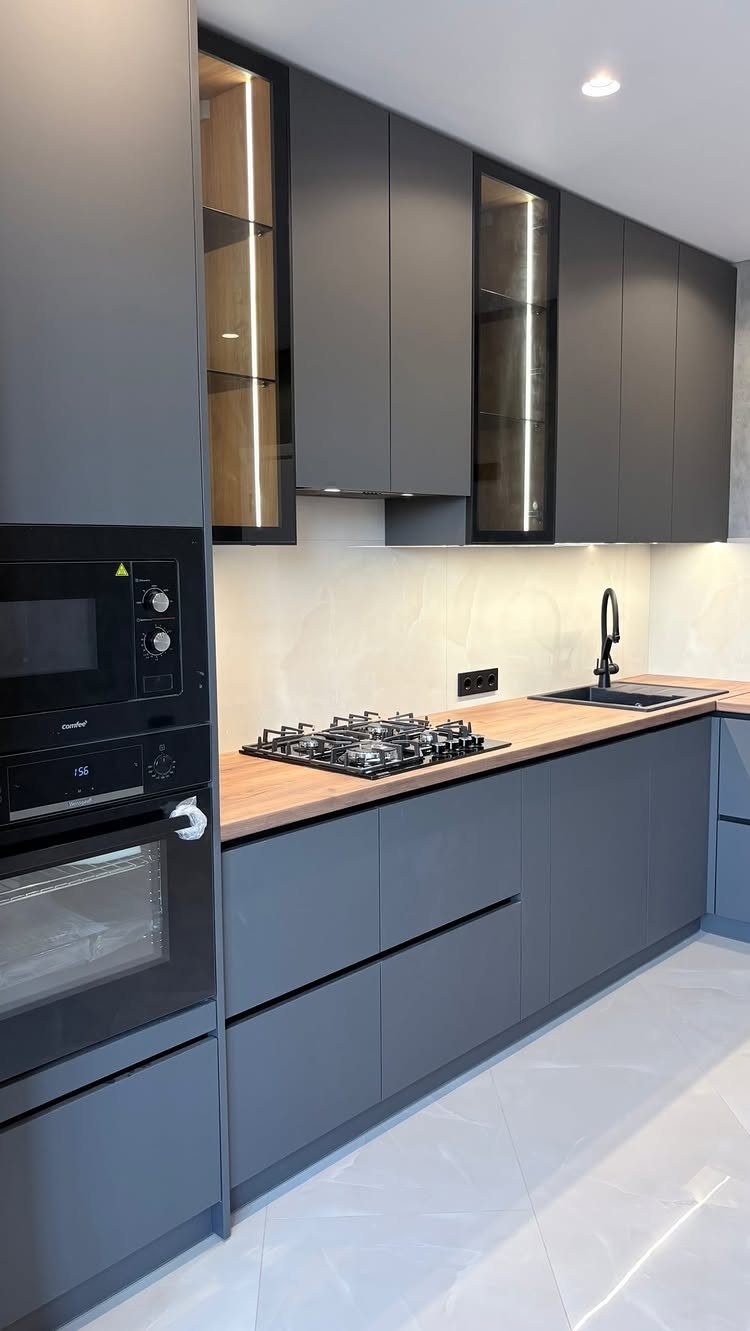 Modern gray kitchen cabinets with light wood countertops and white tiled flooring.
