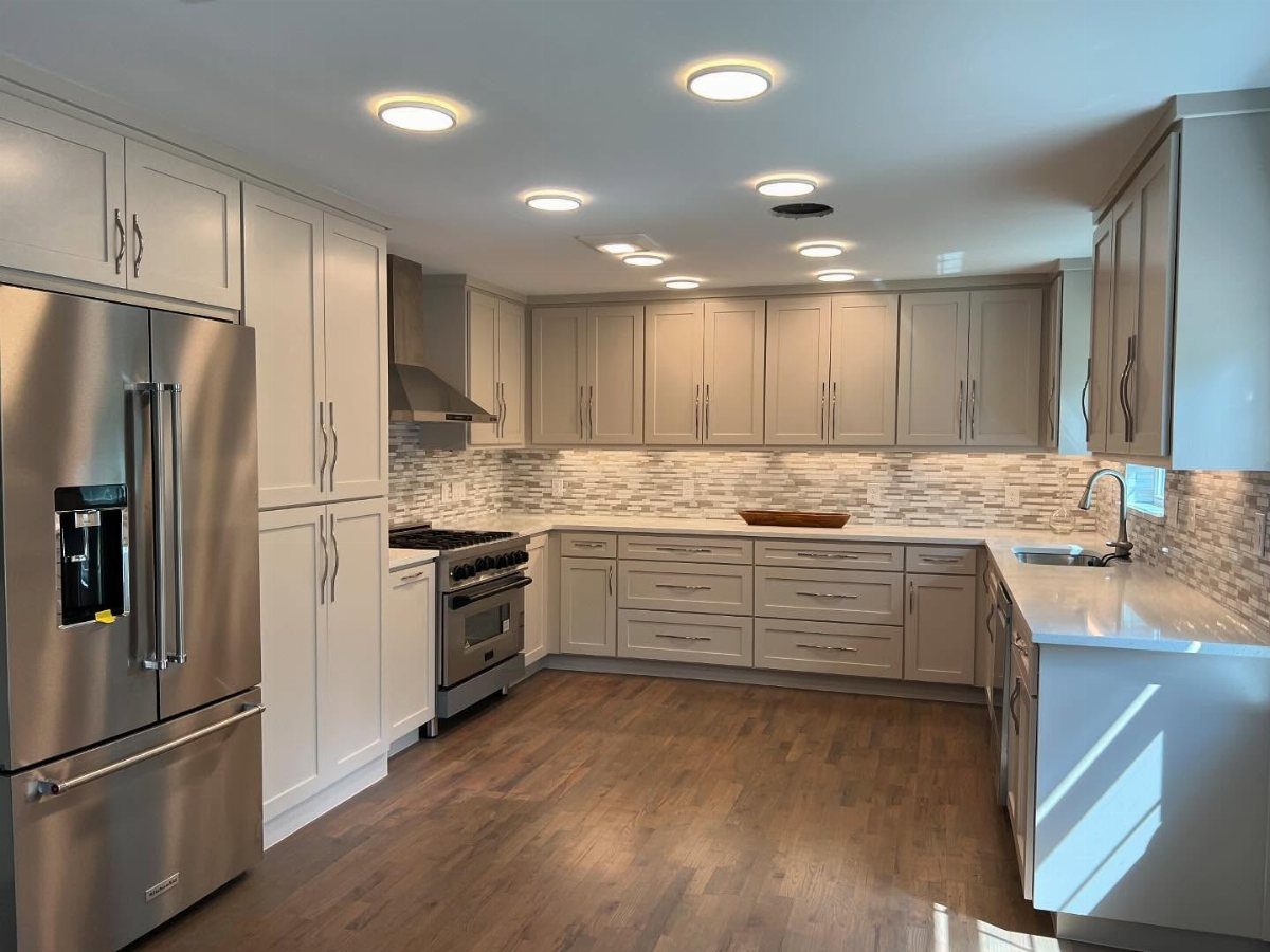 Light gray shaker cabinets with white countertops and a white tiled backsplash in a kitchen.