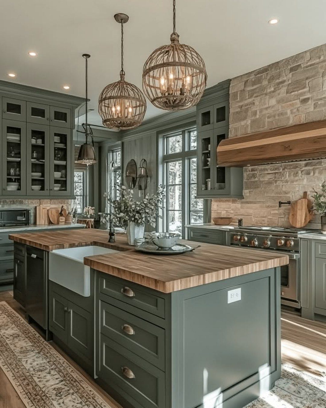 Green-gray kitchen cabinets with a wooden island countertop and spherical woven pendant lights.