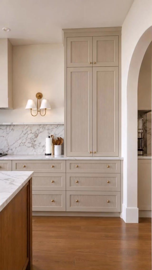 Light gray shaker cabinets with gold hardware and white marble countertops in a kitchen.