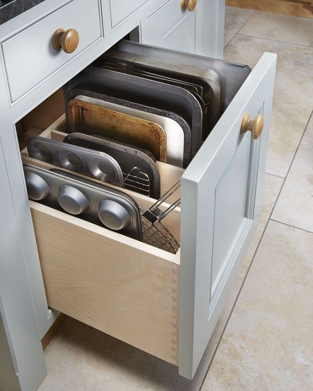 Open grey kitchen drawer with organized baking sheets and muffin tins in dividers.