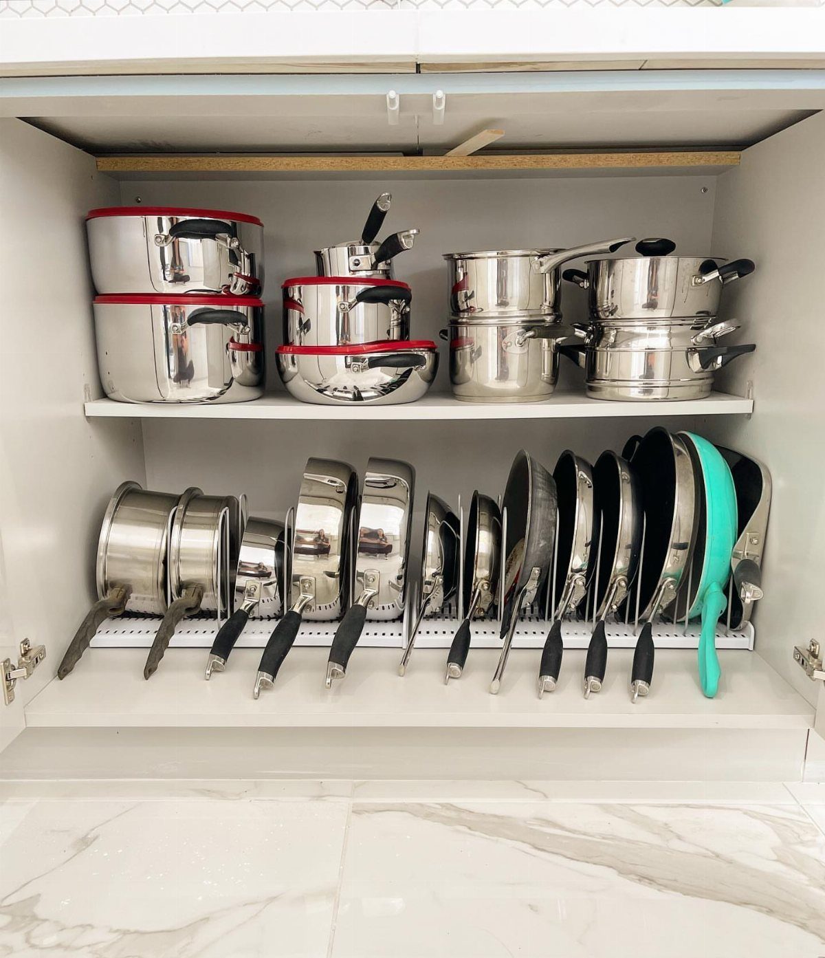 Stainless steel pots and frying pans organized in a white kitchen cabinet shelf.