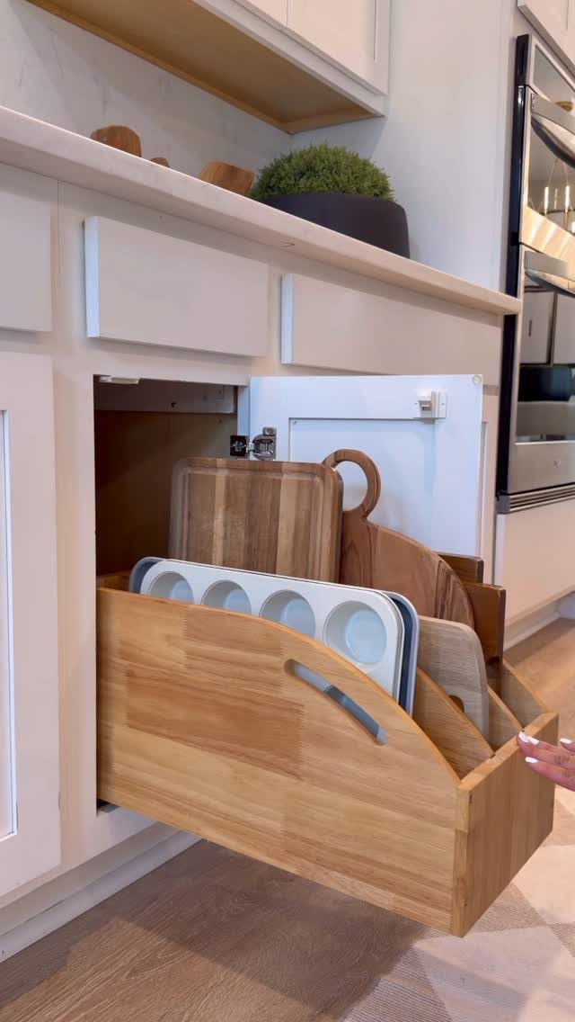 Wooden pull-out kitchen drawer containing cutting boards and white trays in white cabinetry.